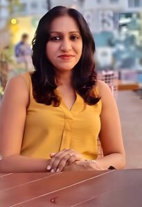 Priya Rao's picture with yellow sleeveless dress and open hair in a cafe with wooden table.